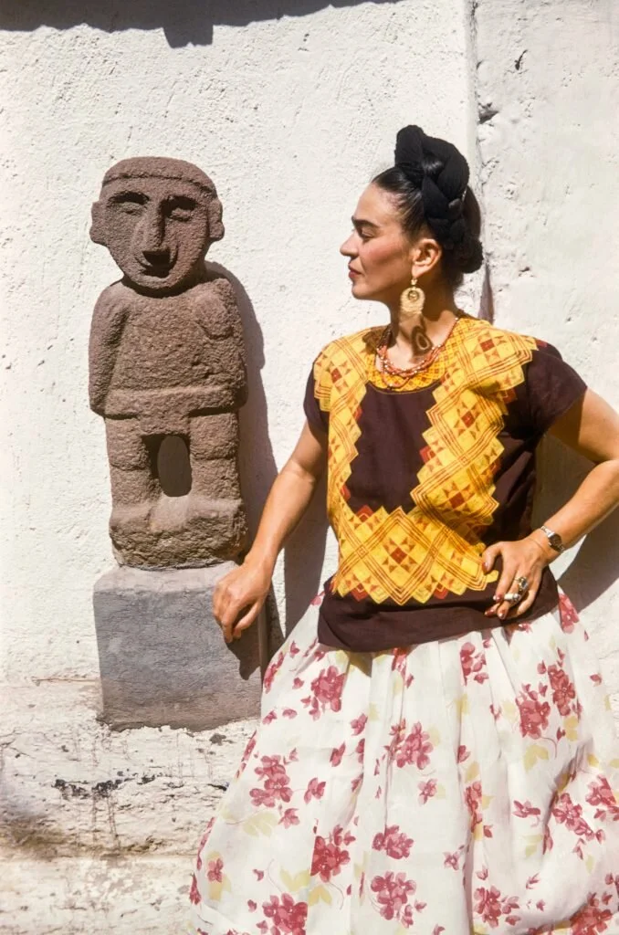 Frida Kahlo beside a Pre-Hispanic sculpture in the garden of the Casa Azul (1951). Photo ©bpk/IMEC, Fonds MCC/Gisèle Freun, ©Banco de Mexico Diego Rivera Frida Kahlo Museums Trust/VG Bild-Kunst, Bonn 2021; reproduction authorized by the Instituto Nacional de Bellas Artes y Literatura, 2021.